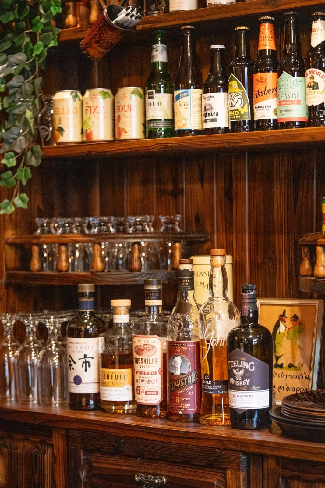 Hyllan i baren med ölflaskor högst upp, glas på hyllorna under och whiskyflaskor på bänken.